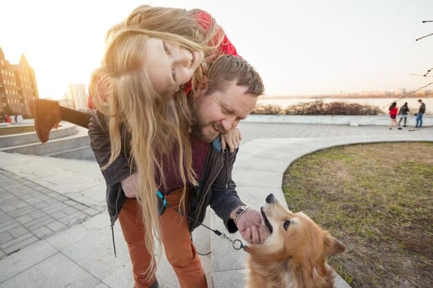 A happy family is reunited with their dog. The family is smiling and hugging the dog, while the dog is visibly happy to be back with its owners. The scene is set in front of their home, with a suburban street in the background.