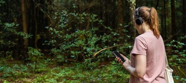 A researcher holding a GPS tracking device, with the background blurred to show a dense forest environment. The researcher is looking at the device screen intently.