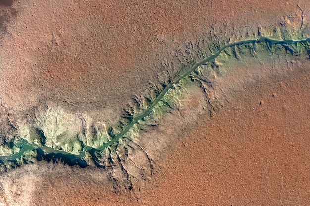 An aerial view of a dried-up riverbed in the southwestern US, illustrating the severe impact of drought on water resources and wildlife habitats. The cracked earth and parched vegetation highlight the urgent need for effective water management strategies. The lighting is harsh and unforgiving, emphasizing the desolation of the landscape.