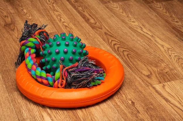 An eye-level shot of a variety of dog chew toys, including rubber bones, rope toys, and puzzle toys, arranged on a wooden surface. The toys are in bright colors and various textures.