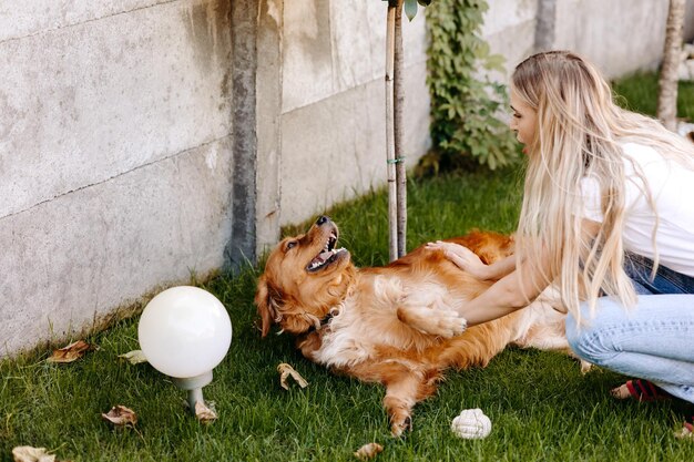 A medium-sized dog is happily playing fetch with a young woman in a fenced backyard. The dog has a bright smile, and the woman is throwing a ball, showcasing a fun and interactive foster environment.